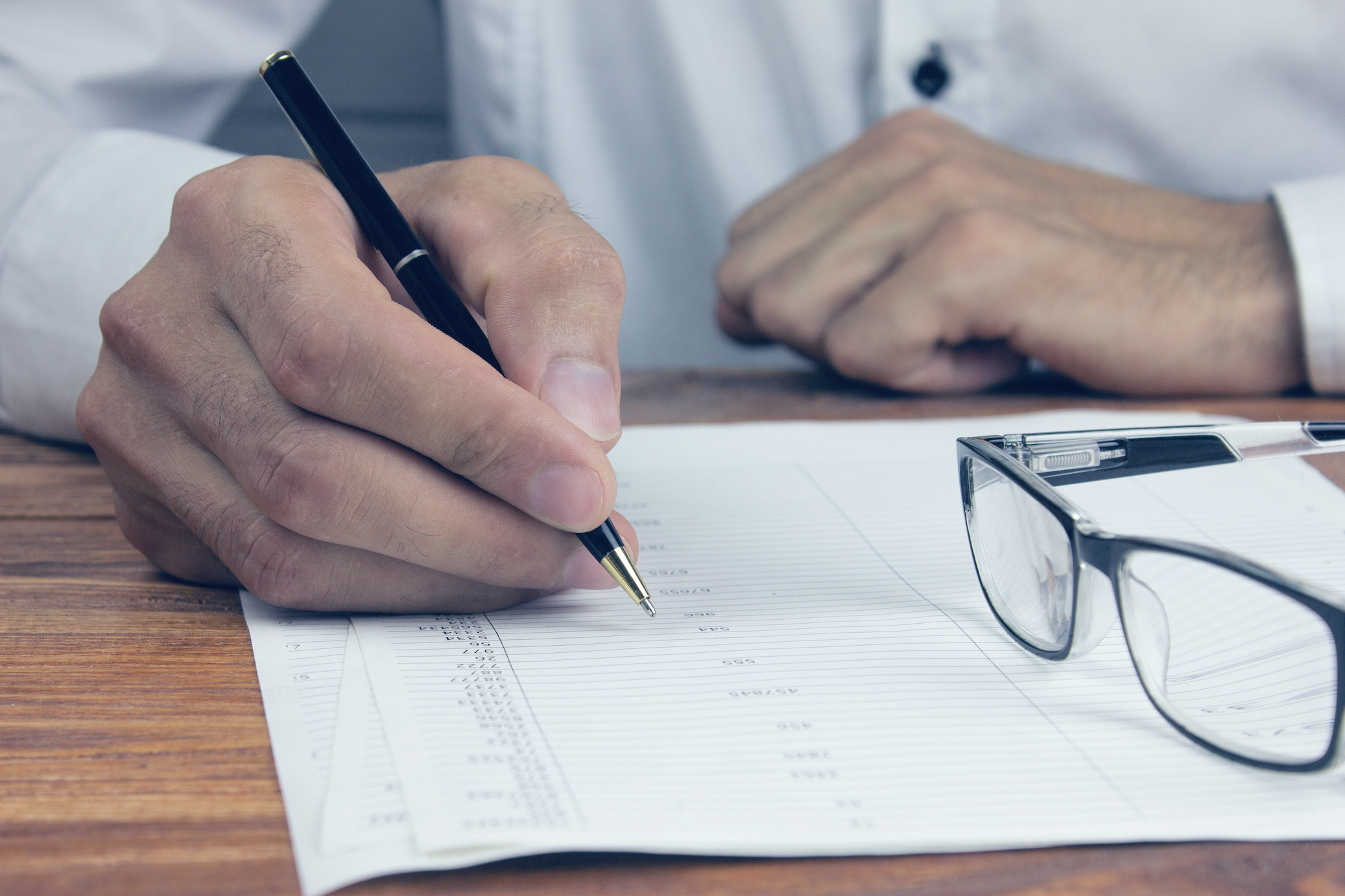 A pair of glasses on a document, with a hand holding a pen guiding the reading of a potential Cureus publication